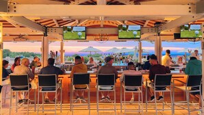 An outdoor bar area with multiple screens displaying sports, surrounded by patrons. - The Mansion at Ocean Edge (Brewster)