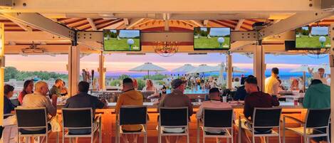 An outdoor bar area with multiple screens displaying sports, surrounded by patrons.