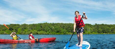 Eine Person steht auf einem Paddleboard auf einem See, im Hintergrund ist ein Wald zu sehen.