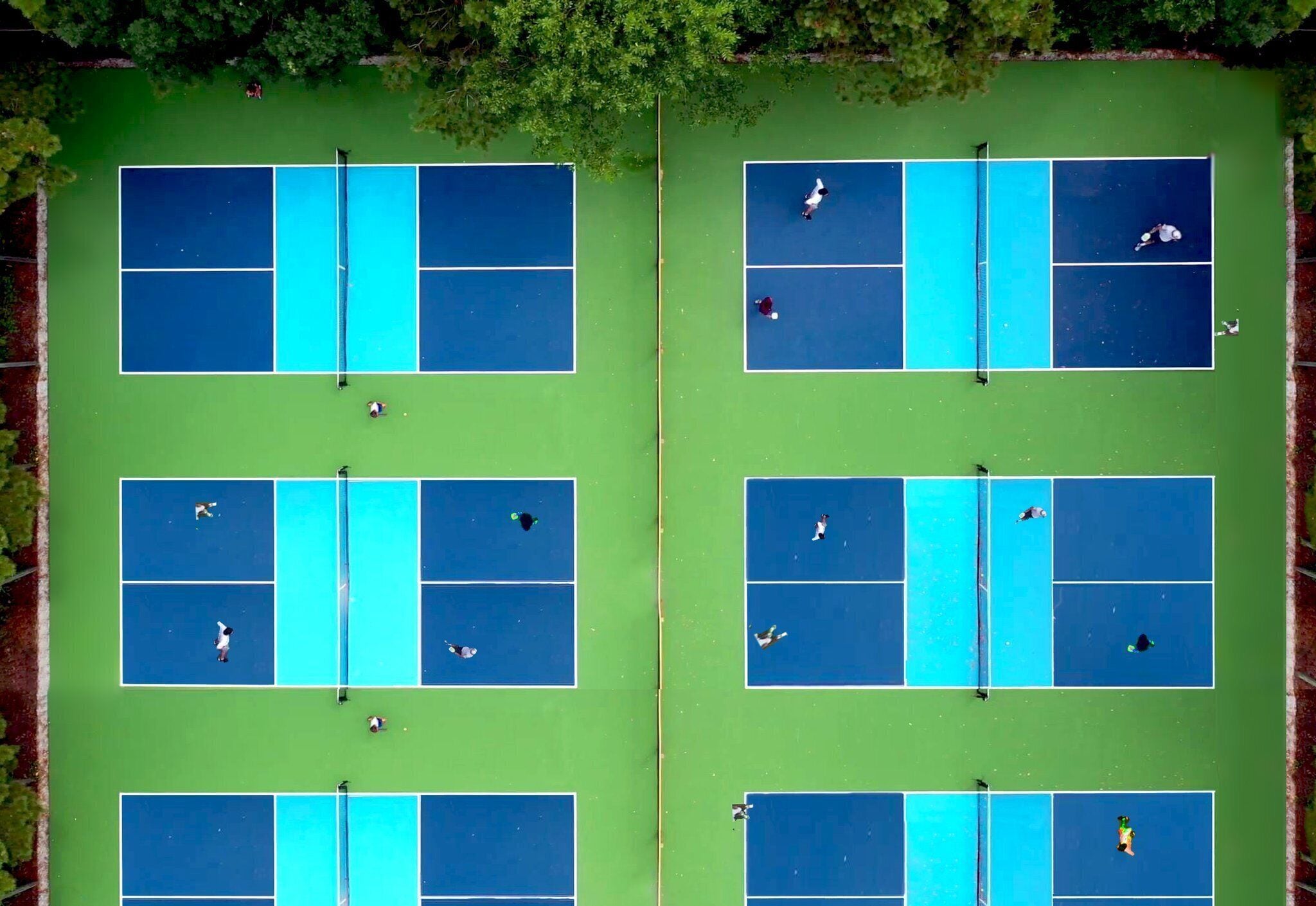 An aerial view of a tennis court complex with multiple courts, a net, and players.