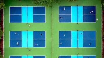 An aerial view of a tennis court complex with multiple courts, a net, and players.