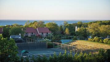 Ein Tennisplatz, von Bäumen und Häusern umgeben, mit Blick auf das Meer.