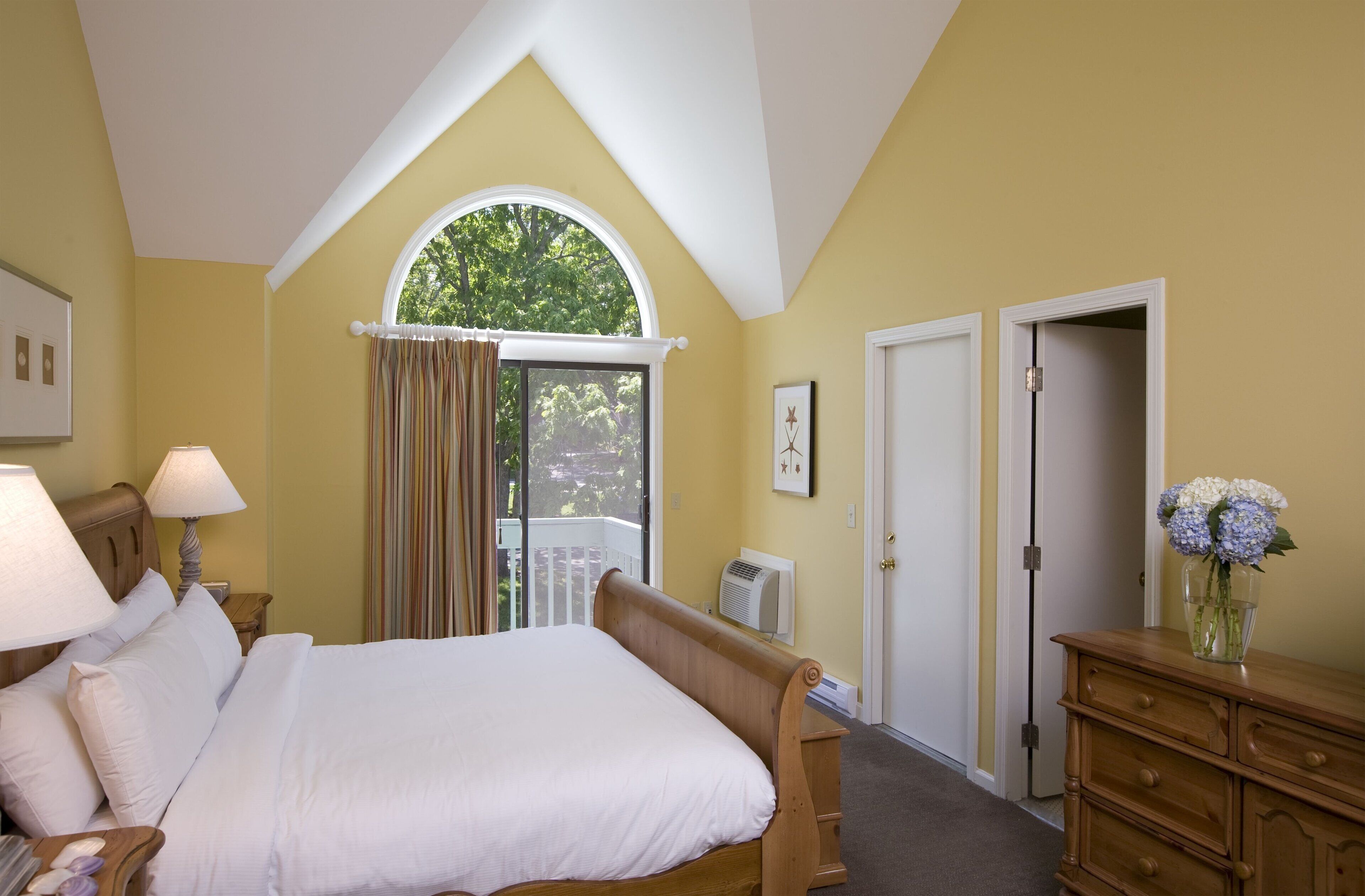 Une chambre à coucher avec un grand lit, une fenêtre avec des rideaux, une commode et une porte.