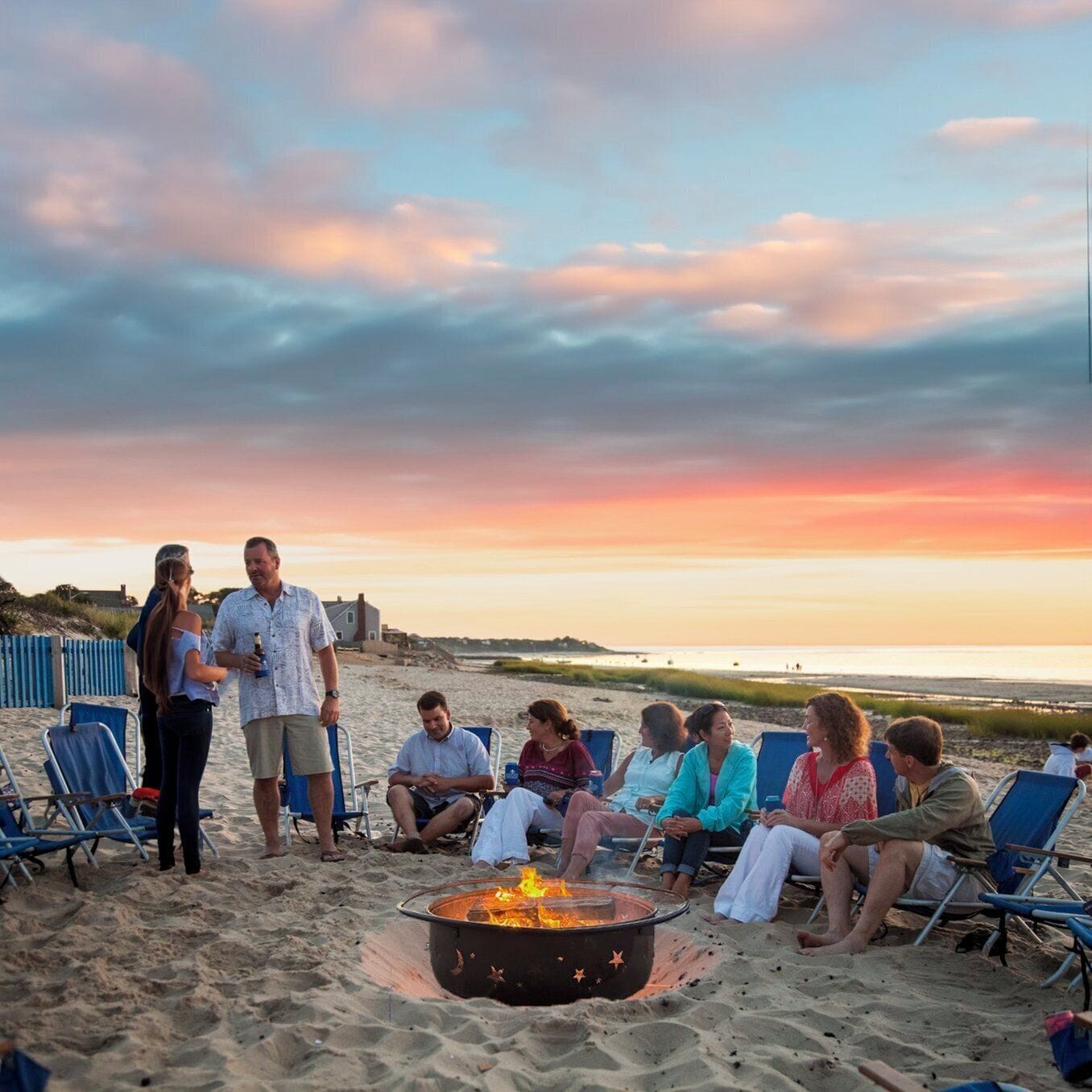 Un grupo de personas reunidas alrededor de una fogata en la playa al atardecer.