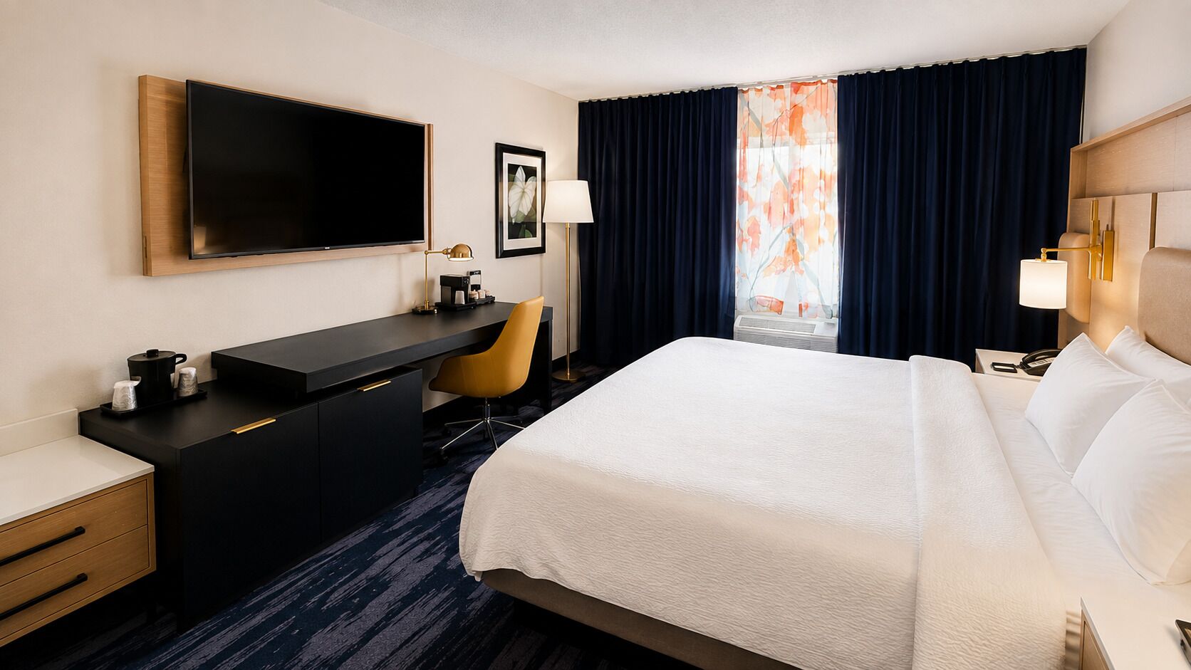 Une chambre d’hôtel avec un grand lit, un bureau doté d’un téléviseur à écran plat, une chaise et une fenêtre avec des rideaux.