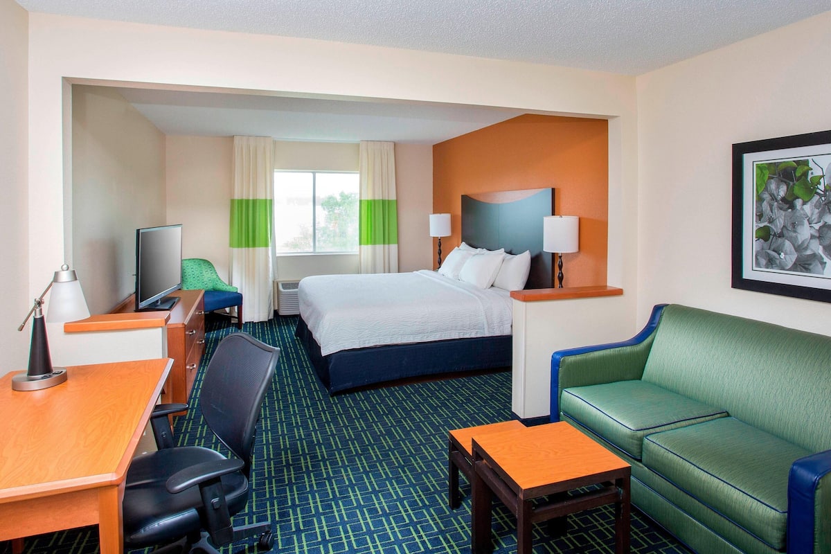 A hotel room with a bed, a desk, a chair, a sofa, and a television.
