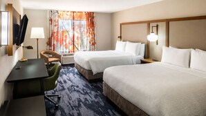 Een hotelkamer met twee bedden, een bureau, een stoel, een televisie en een raam met gordijnen.