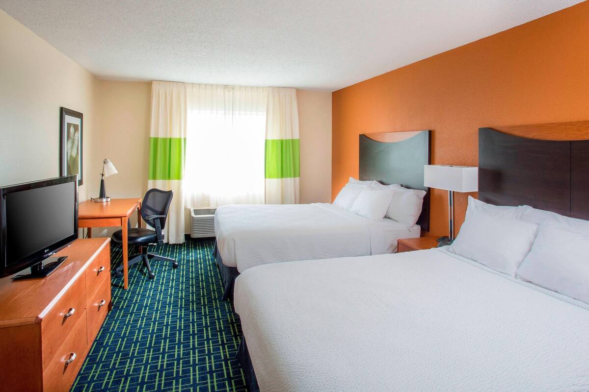 A hotel room with two beds, a desk with a television, and a chair.