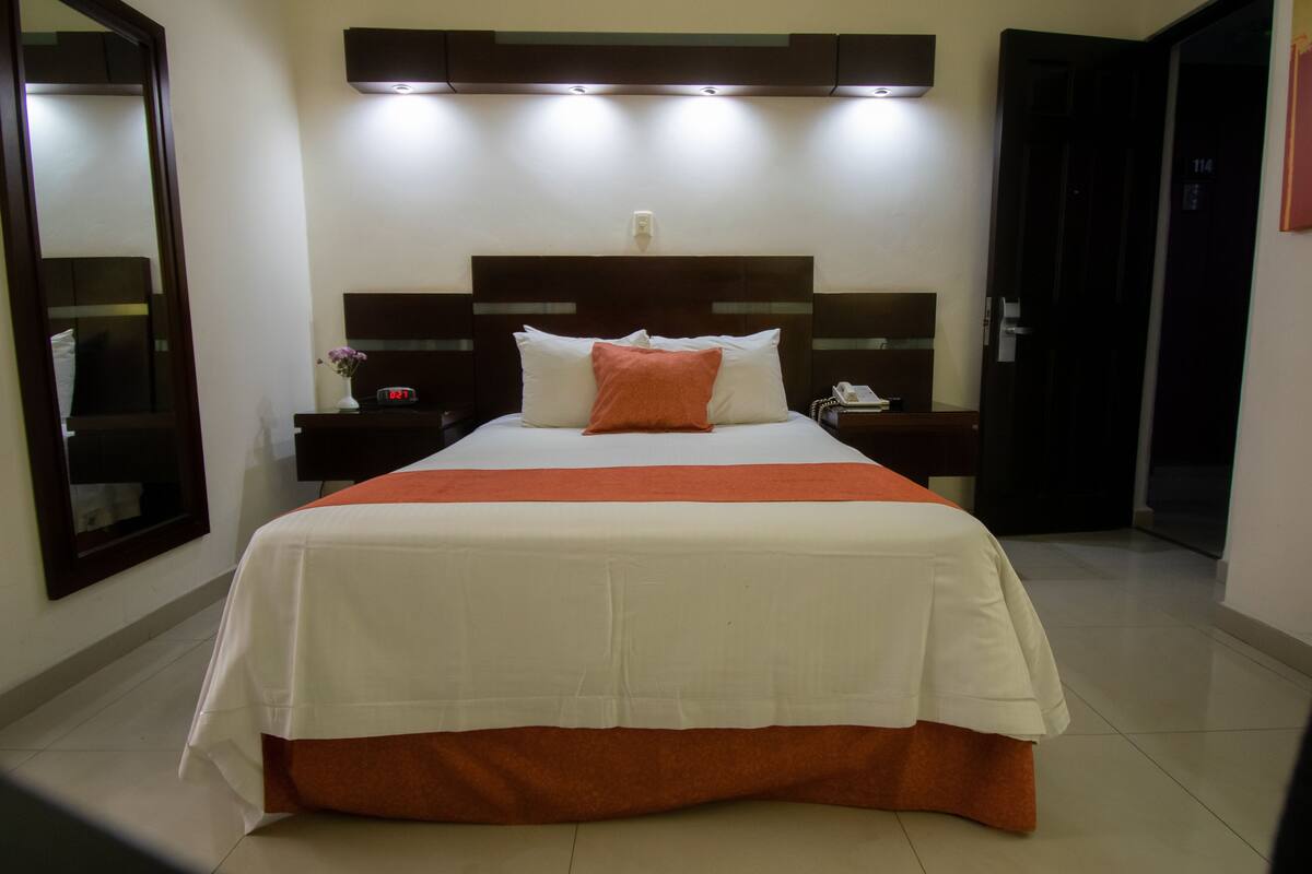 A hotel room with a large bed, a nightstand with a lamp, and a mirror.