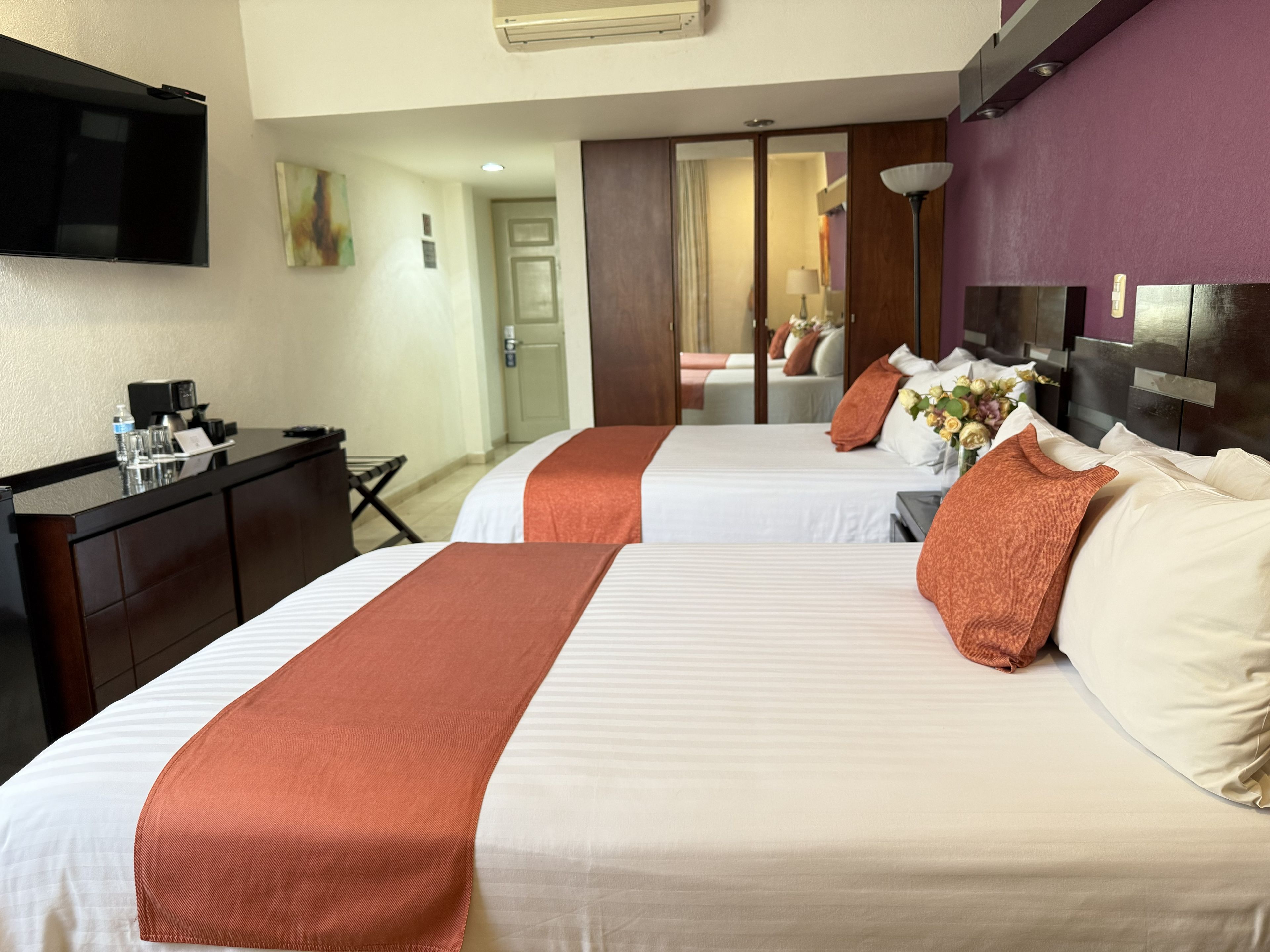 A hotel room with two beds, a desk, a television, and a mirror.