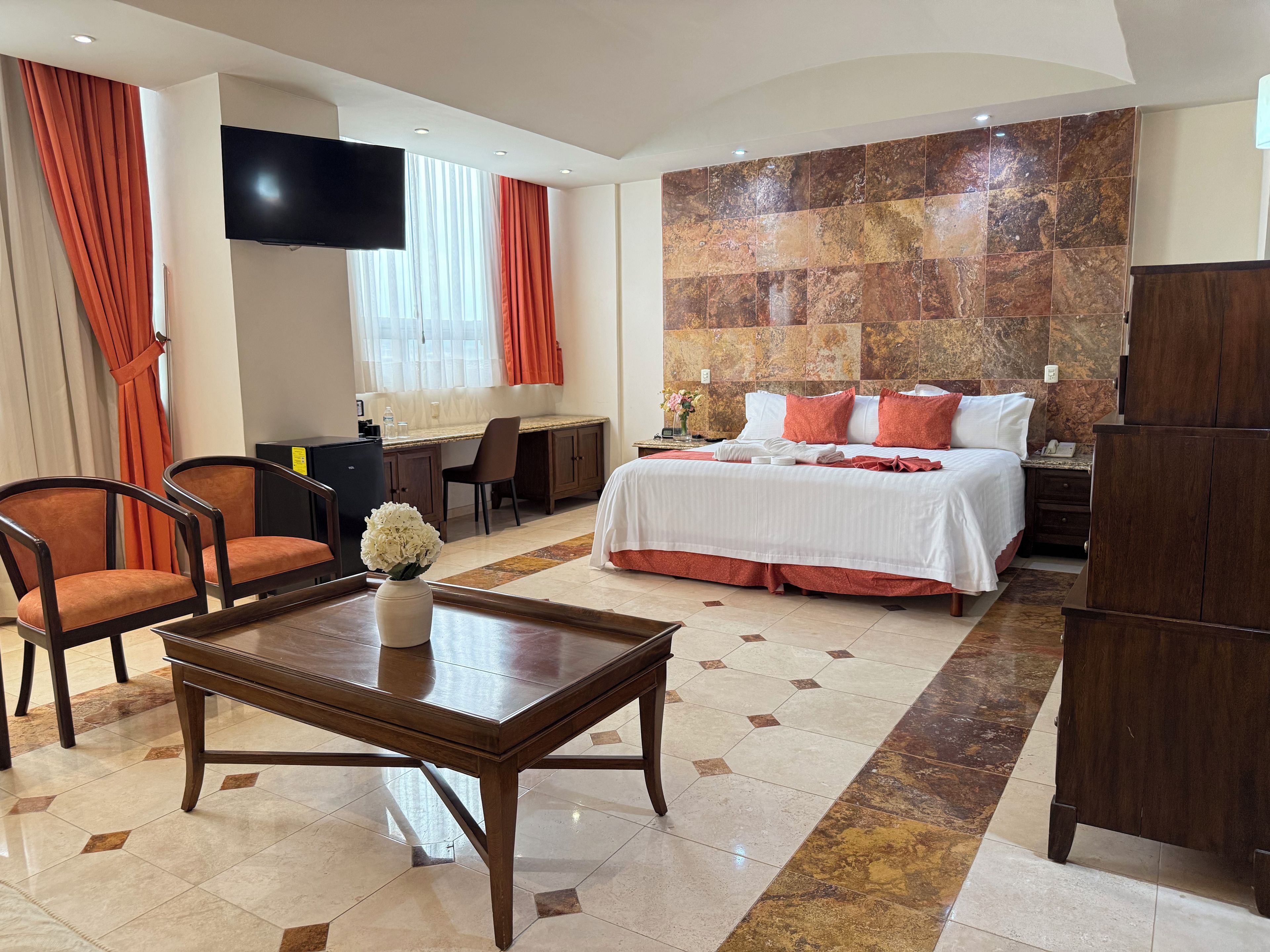 A hotel room with a bed, a desk, a chair, a TV, and a large stone wall.