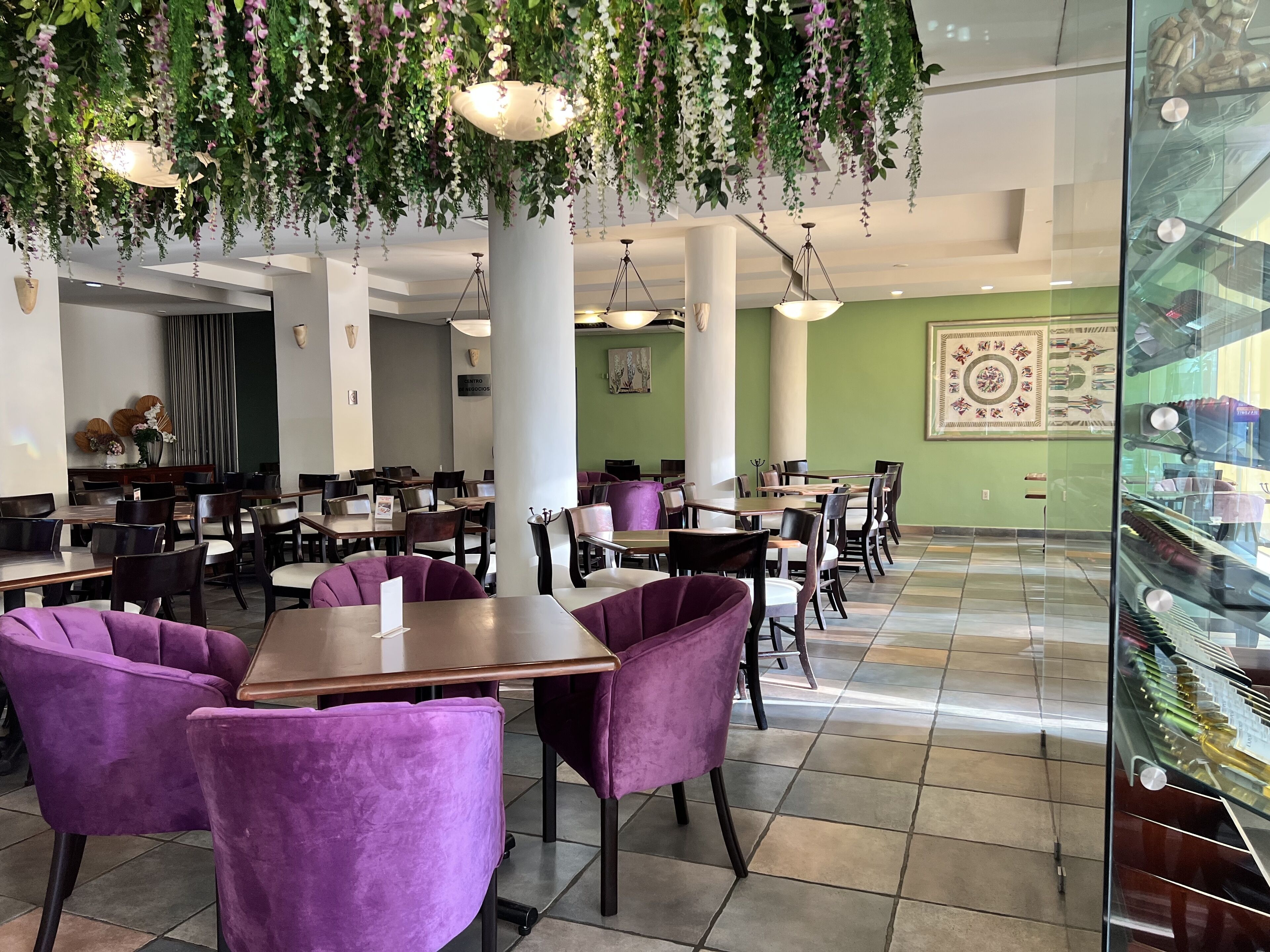 Een restaurant met paarse stoelen, hangplanten en een groene muur met een decoratief patroon.