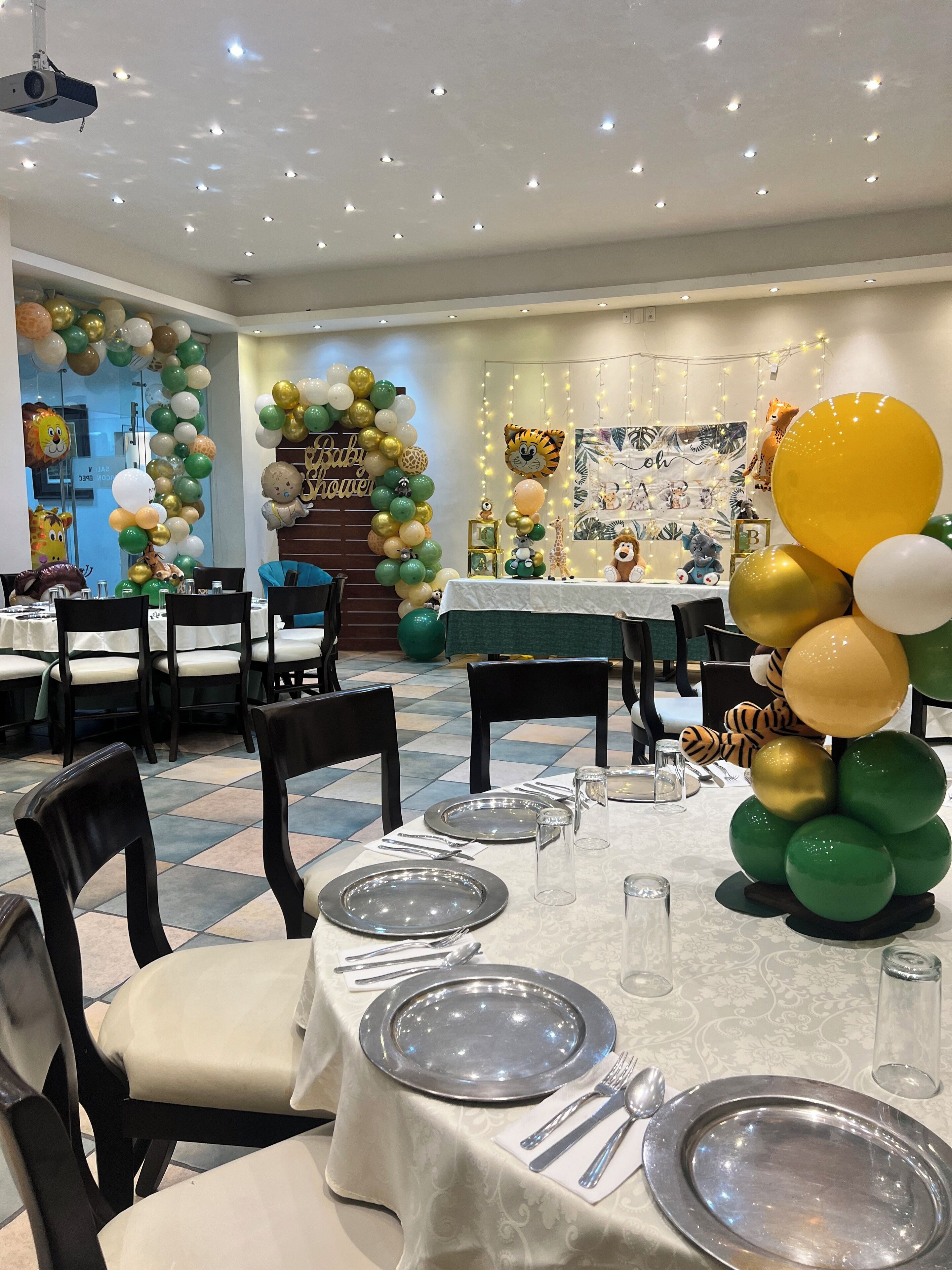 A banquet hall with tables set for a baby shower, decorated with balloons and themed wall hangings.