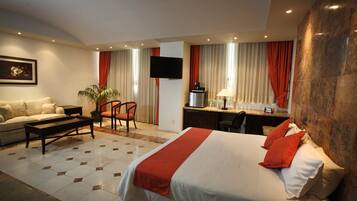 Ein Hotelzimmer mit einem großen Bett, einer Sitzecke, einem Schreibtisch und einem Fernseher.