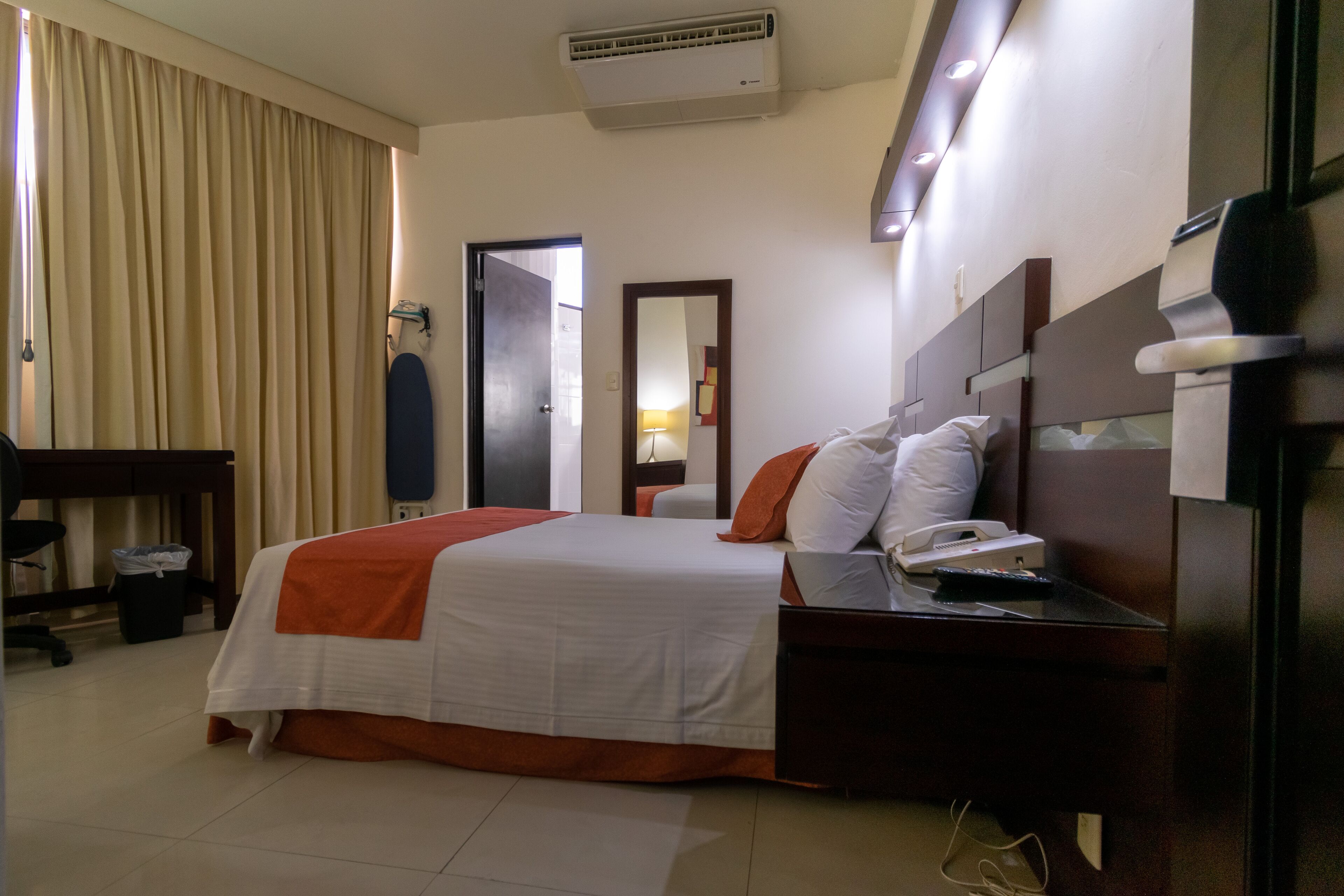 A hotel room with a bed, bedside table, lamp, and a mirror.