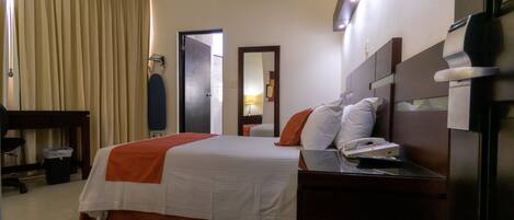 A hotel room with a bed, bedside table, lamp, and a mirror.