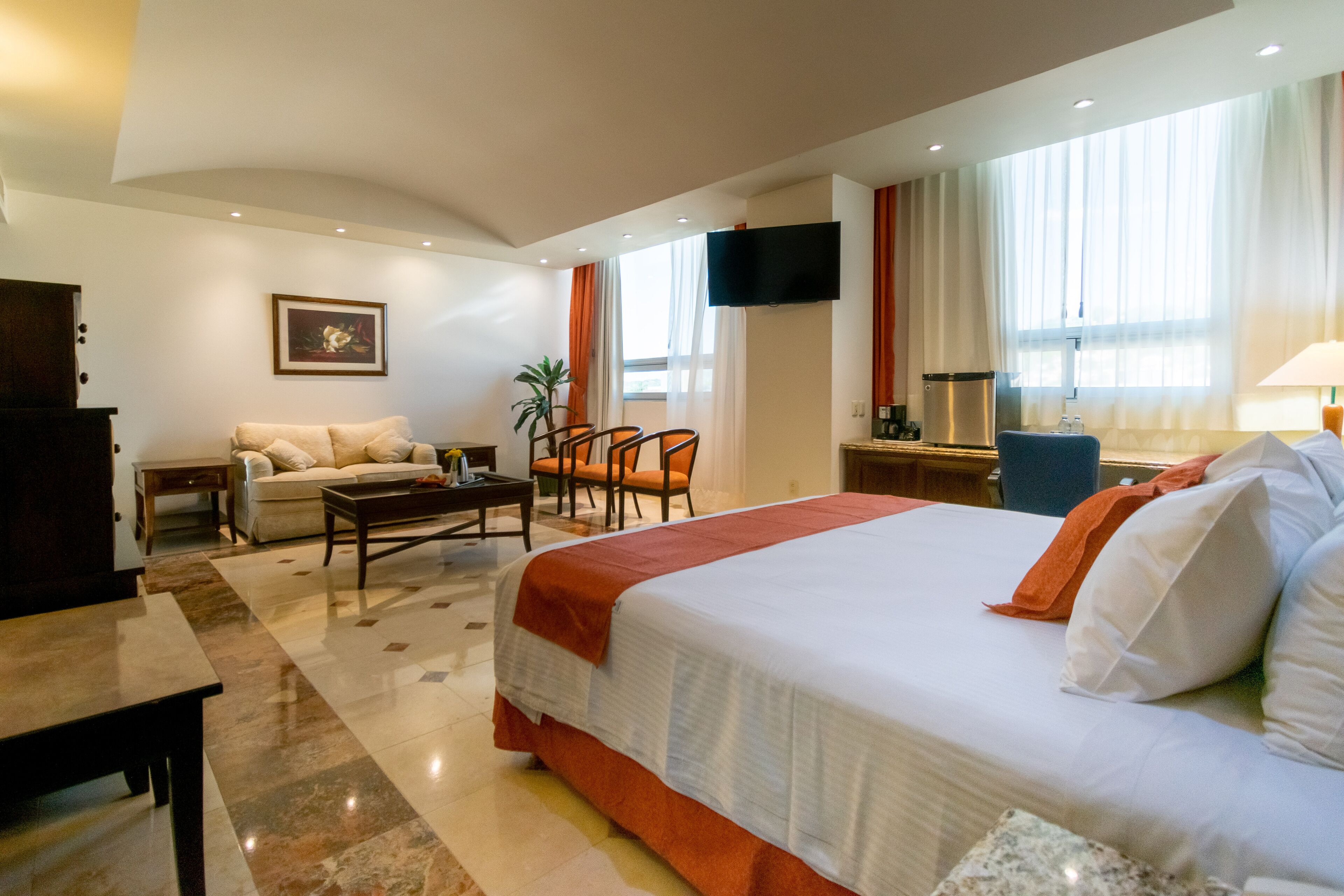 A hotel room with a bed, a sofa, a desk, a TV, and a window with curtains.