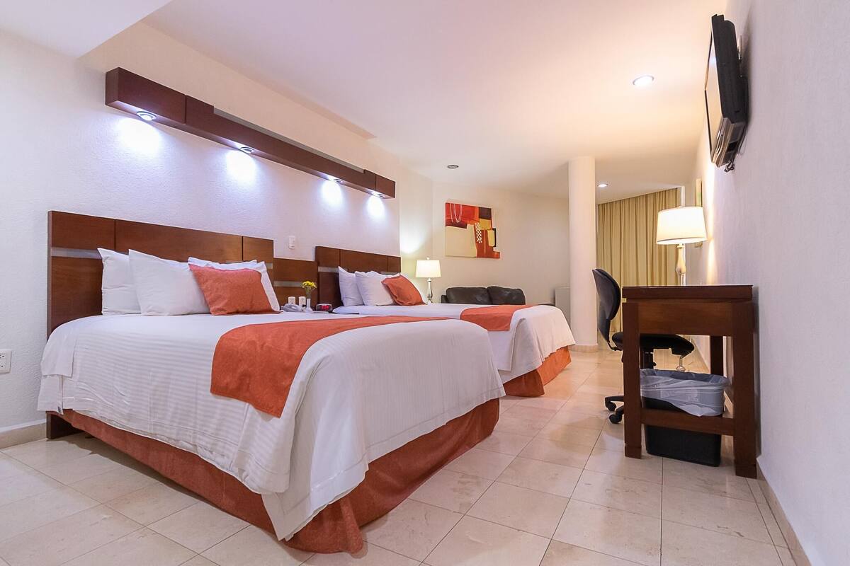 A hotel room with two beds, a TV, a desk, and a lamp.
