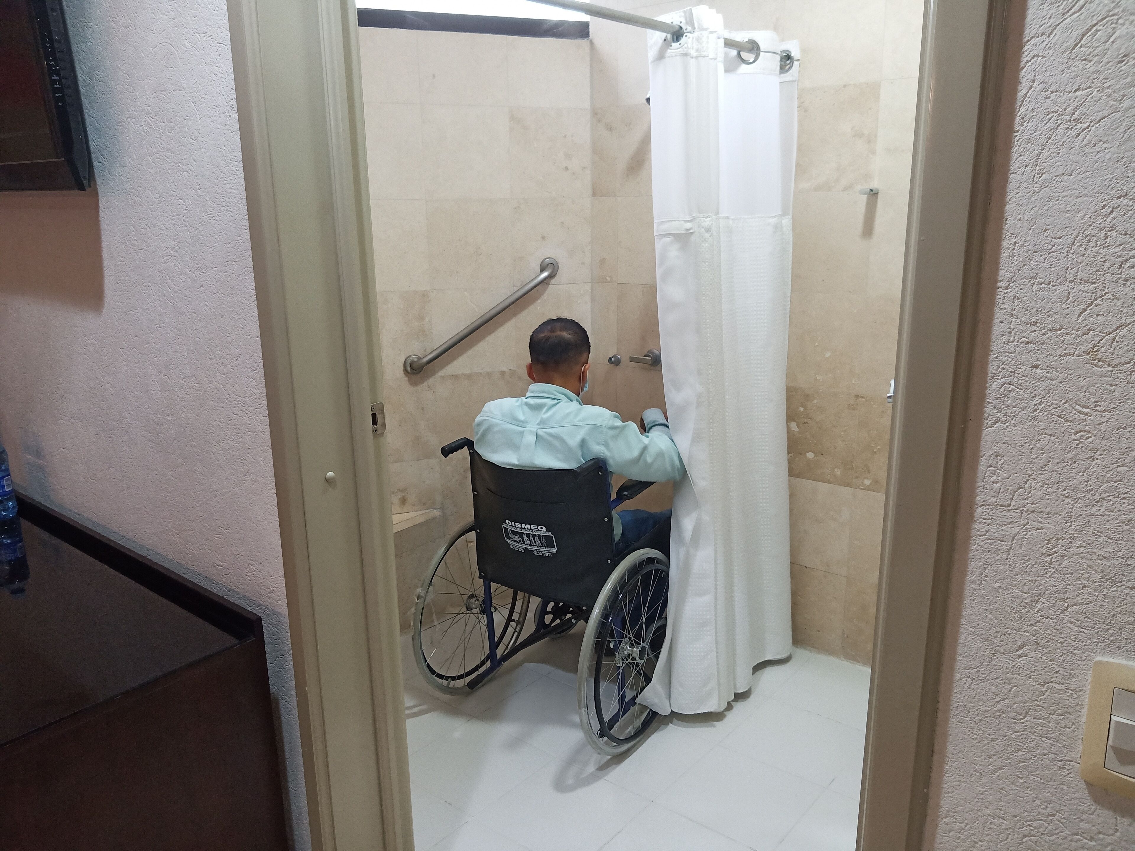 A wheelchair-accessible shower area with a white curtain, a handrail, and a tiled floor.