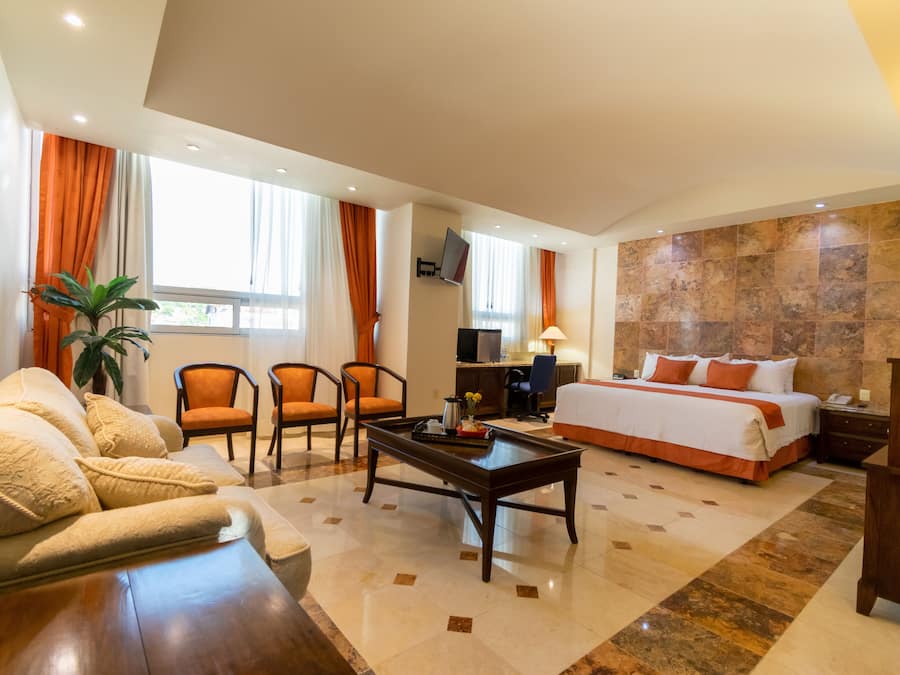 A hotel room with a bed, a seating area with chairs, a coffee table, a TV, and a large window with curtains.