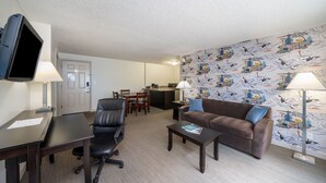 A furnished living room with a desk, a couch, a TV, and a patterned wall. - The Grove West Seattle Inn (Seattle)