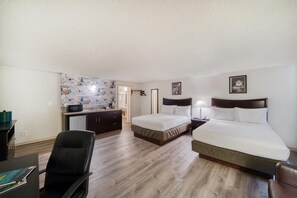 A hotel room with a large bed, a smaller bed, a desk with a chair, a kitchenette, and a bathroom.