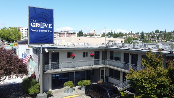 A building with a large blue sign for The Grove West Seattle Inn, featuring a balcony with potted plants and a parking area with a black car.