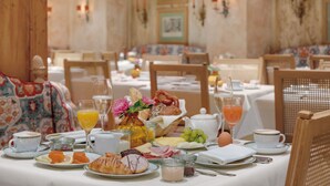 A breakfast setting with various food items, drinks, and a basket of bread on a table. - Hotel Excelsior München (Munich)