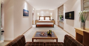 A modern hotel room with a large bed, a small table with candles, a TV, and a view of the city.