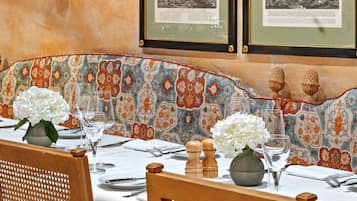 Un área de comedor con un banco estampado, una mesa con vasos y cubiertos, y fotografías en blanco y negro del paisaje enmarcadas en la pared.