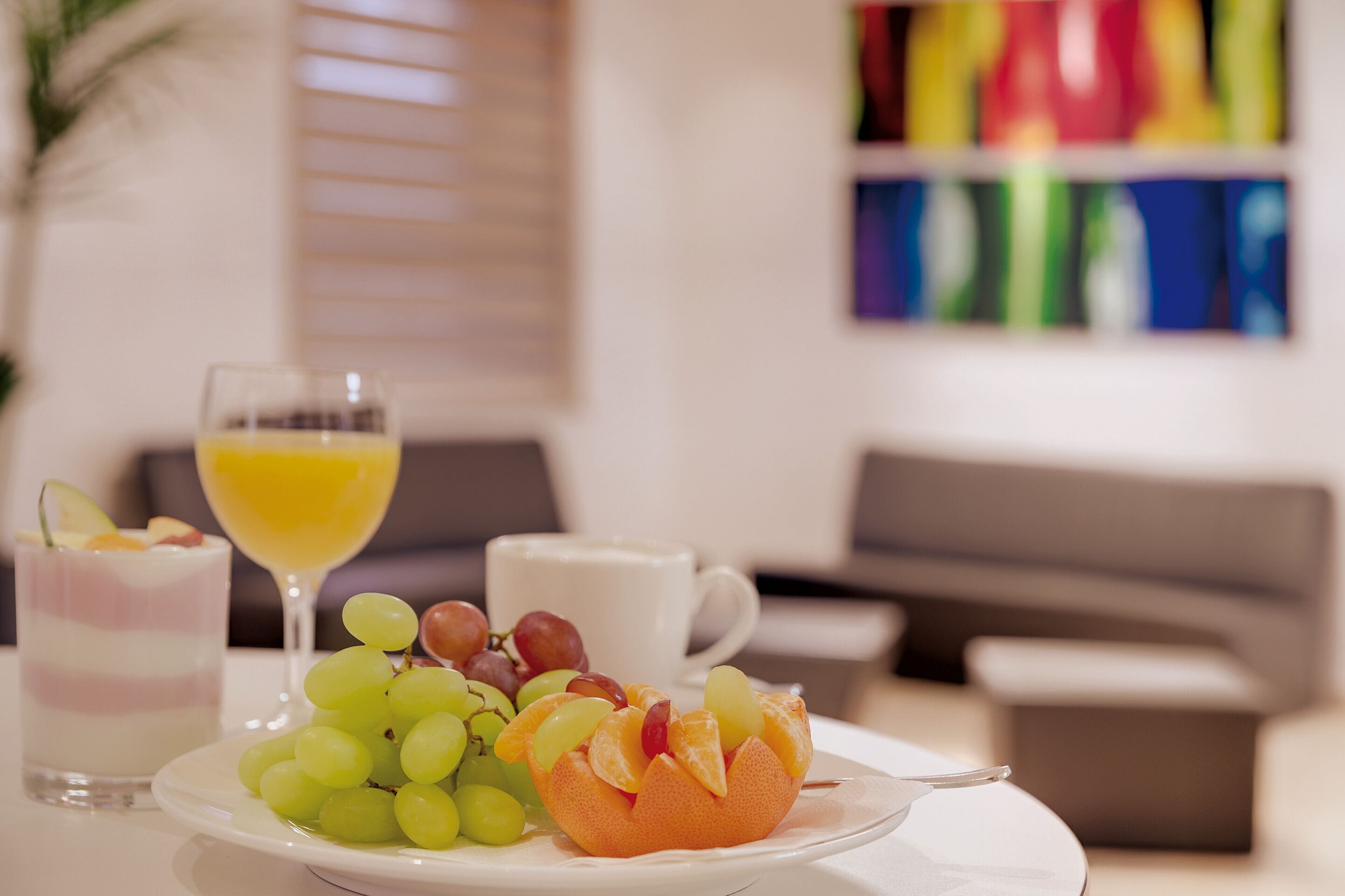 A breakfast setting with a plate of fruit, a glass of orange juice, and a white cup on a table.