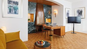 A modern living room with a wooden desk, a television, and framed pictures on the walls. - Hotel Excelsior München (Munich)