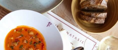 A table with a bowl of soup, a plate of salad, a basket of bread, and a glass of white wine.