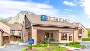 Un hotel Baymont Inn & Suites con un letrero del río Provo, que presenta fachada de ladrillo, una zona de estar exterior cubierta y un telón de fondo de montañas.