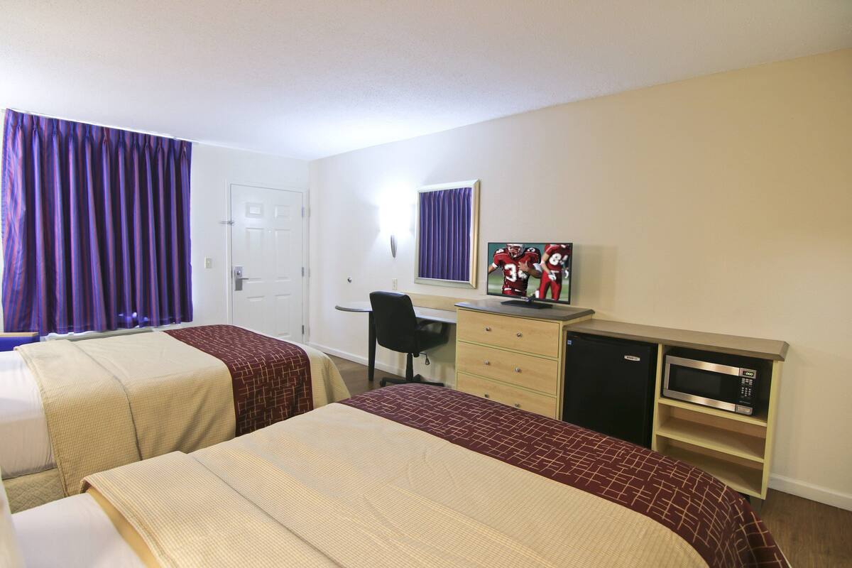 A hotel room with two beds, a desk, a chair, a television, and a microwave.