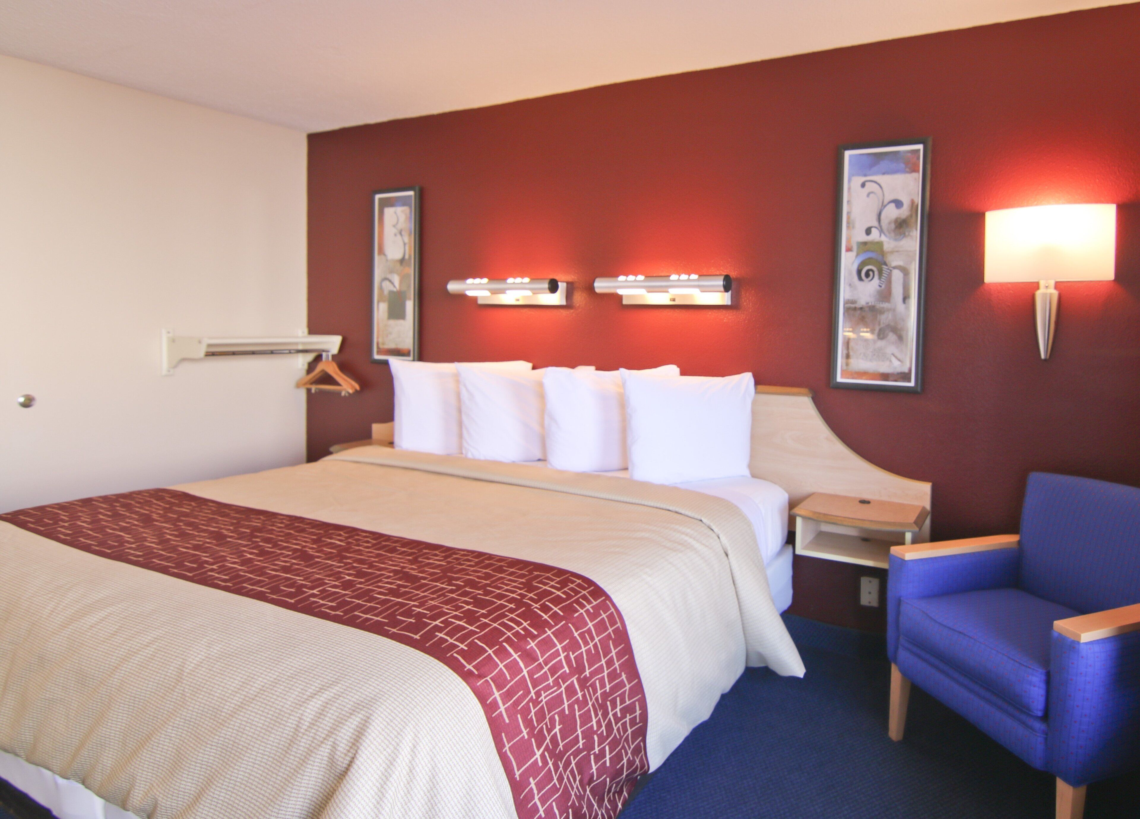 A hotel room with a large bed, a bedside table, a chair, and wall-mounted lamps.