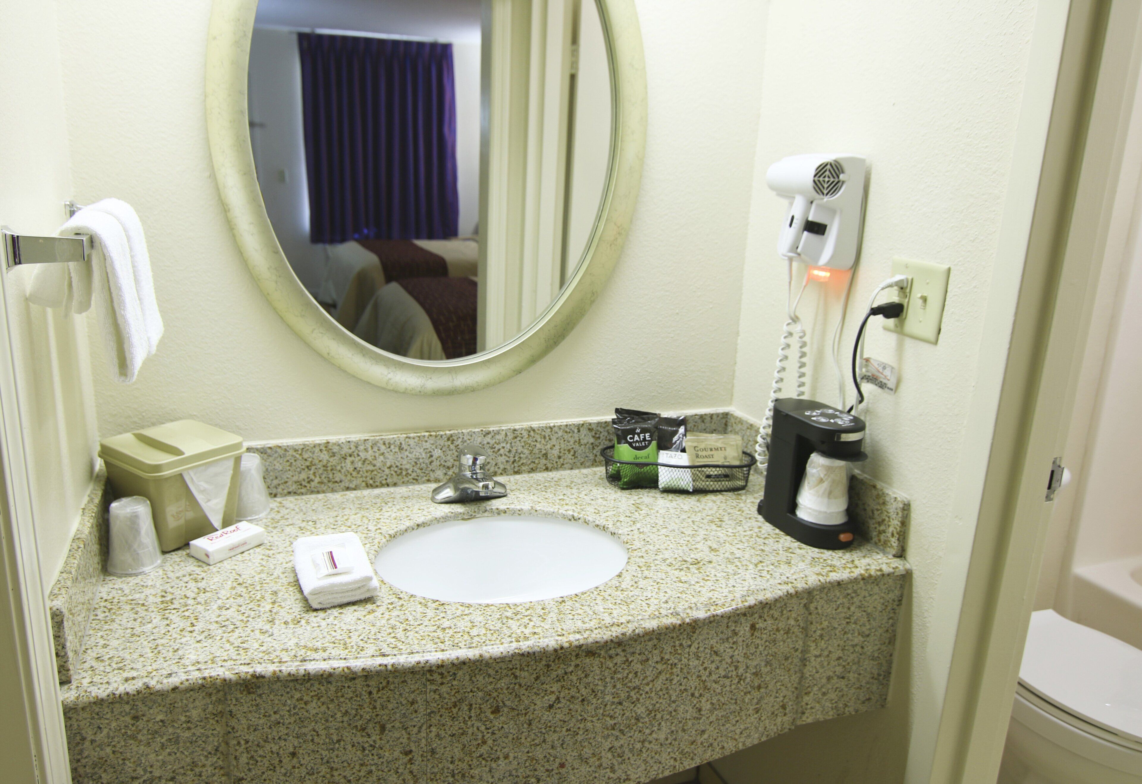 A hotel bathroom with a sink, mirror, towel rack, and toiletries.