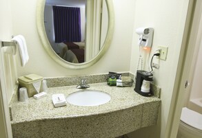 Un baño de hotel con lavamanos, espejo, toallero y artículos de aseo.