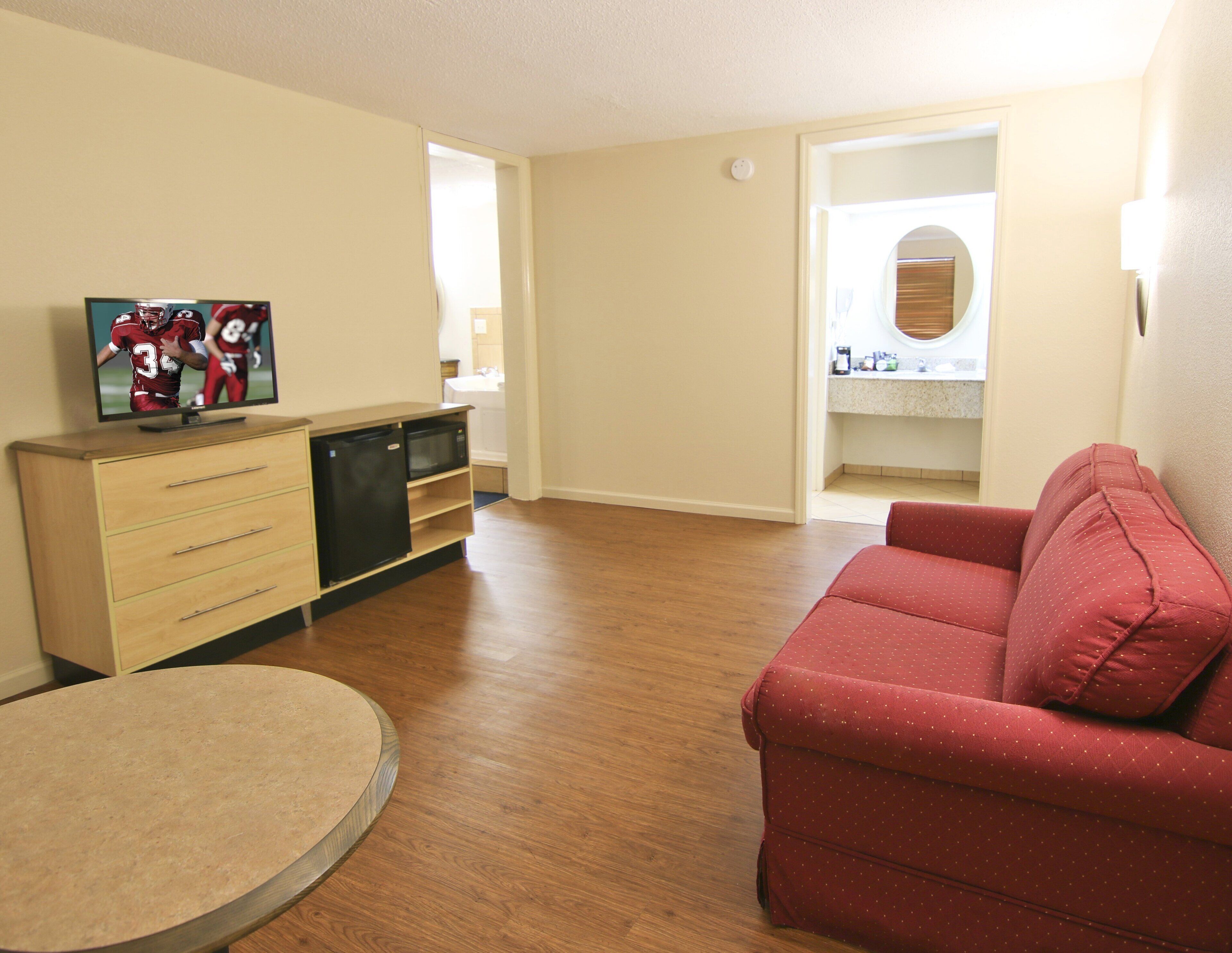 A living room with a red sofa, a television on a wooden cabinet, and a round table.