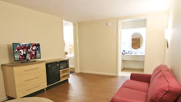 A living room with a red sofa, a television on a wooden cabinet, and a round table.