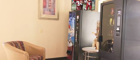 A room with a patterned armchair, a refrigerator, and a television mounted on the wall.