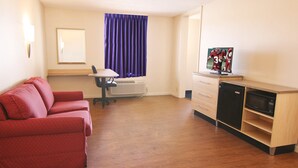 A compact room with a red sofa, a desk with a chair, a microwave, and a small refrigerator. - Red Roof Inn Somerset, KY (Somerset)