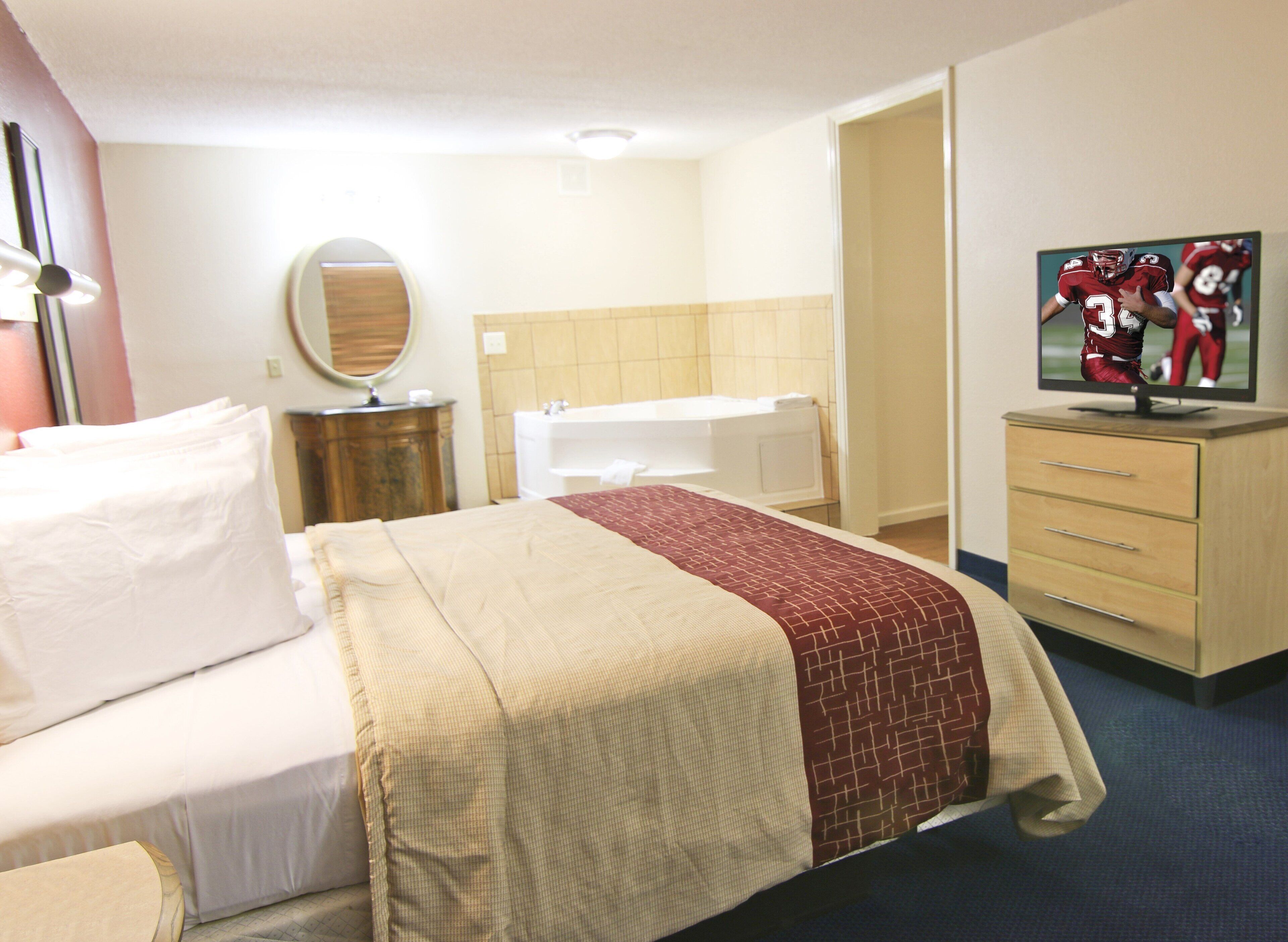 Ein Hotelzimmer mit einem Bett, einem Schminktisch, einem Spiegel, einem Fernseher und einem Badezimmer.