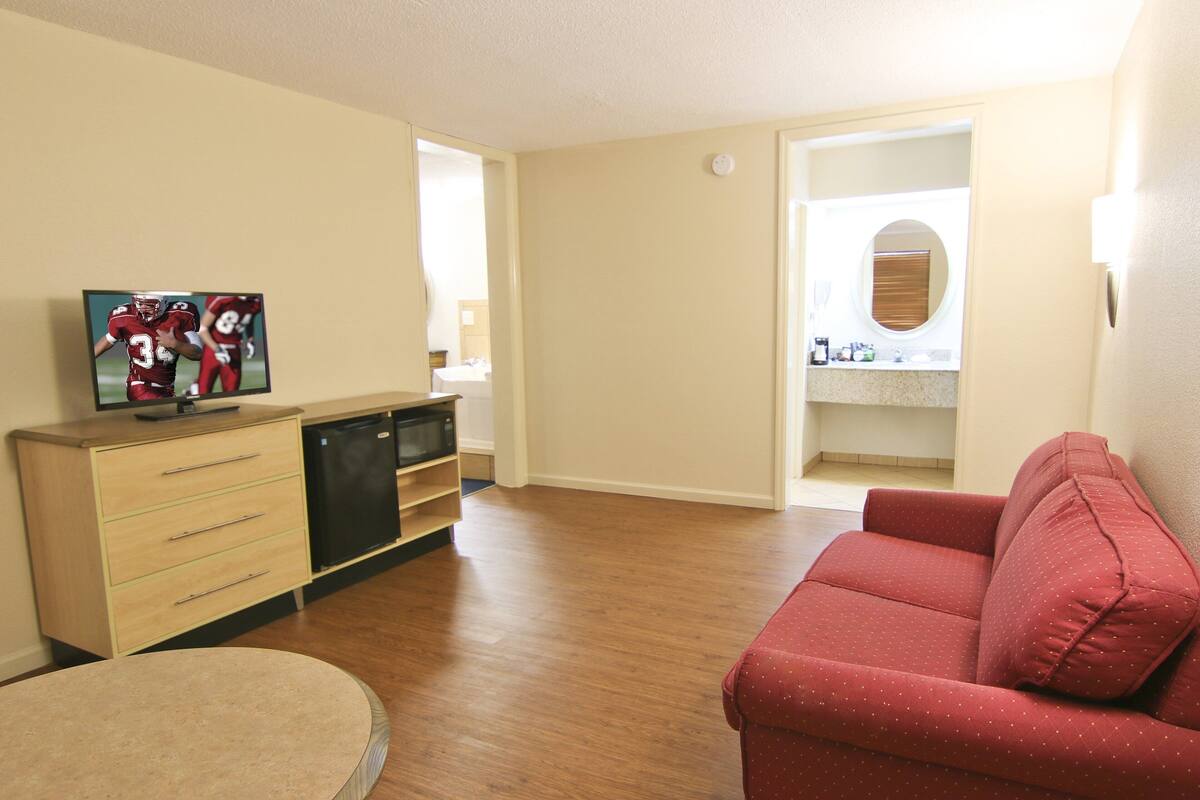 A living room with a red sofa, a wooden cabinet with a flat-screen TV, and a round table.