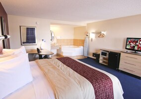 Habitación de hotel con cama, escritorio, silla, televisor y baño con bañera, además de un escritorio con cajones.