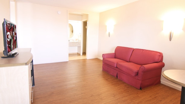 Une pièce avec un plancher en bois, un canapé rouge, une petite table et un luminaire fixé au mur.