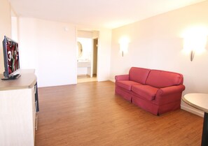 A room with a wooden floor, a red sofa, a small table, and a wall-mounted light fixture.