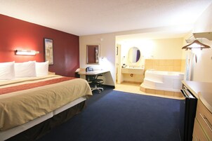 Habitación de hotel con dos camas, un escritorio, una silla, un espejo redondo, un lavamanos y una bañera.