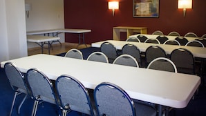 Une salle de conférence dotée de plusieurs tables et chaises, et équipée de lampes fixées aux murs.