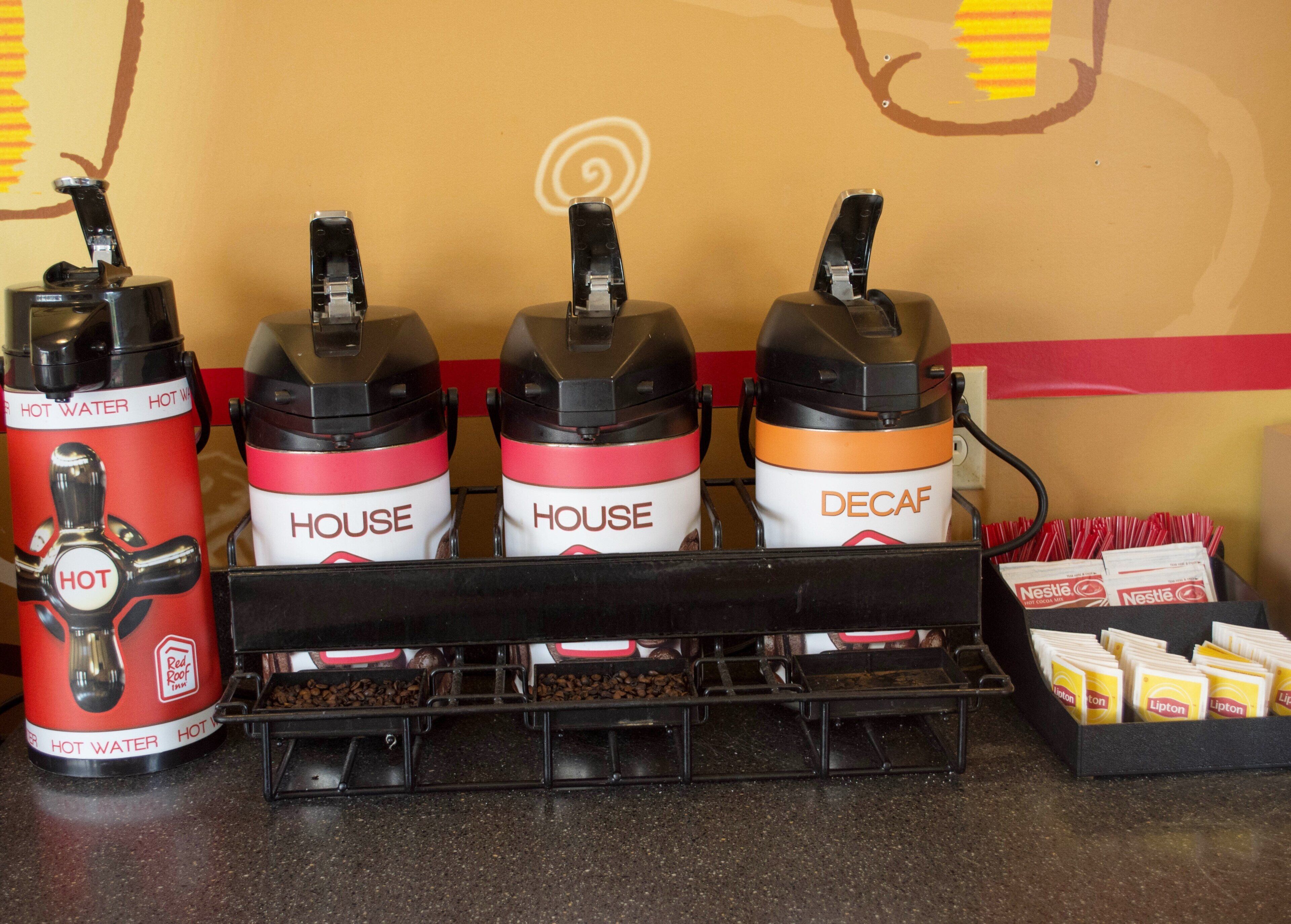 Een koffiehoek met drie koffieautomaten, waarvan er twee 'HOUSE' en 'DECAF' staan, en een rode automaat voor 'HEET WATER'.